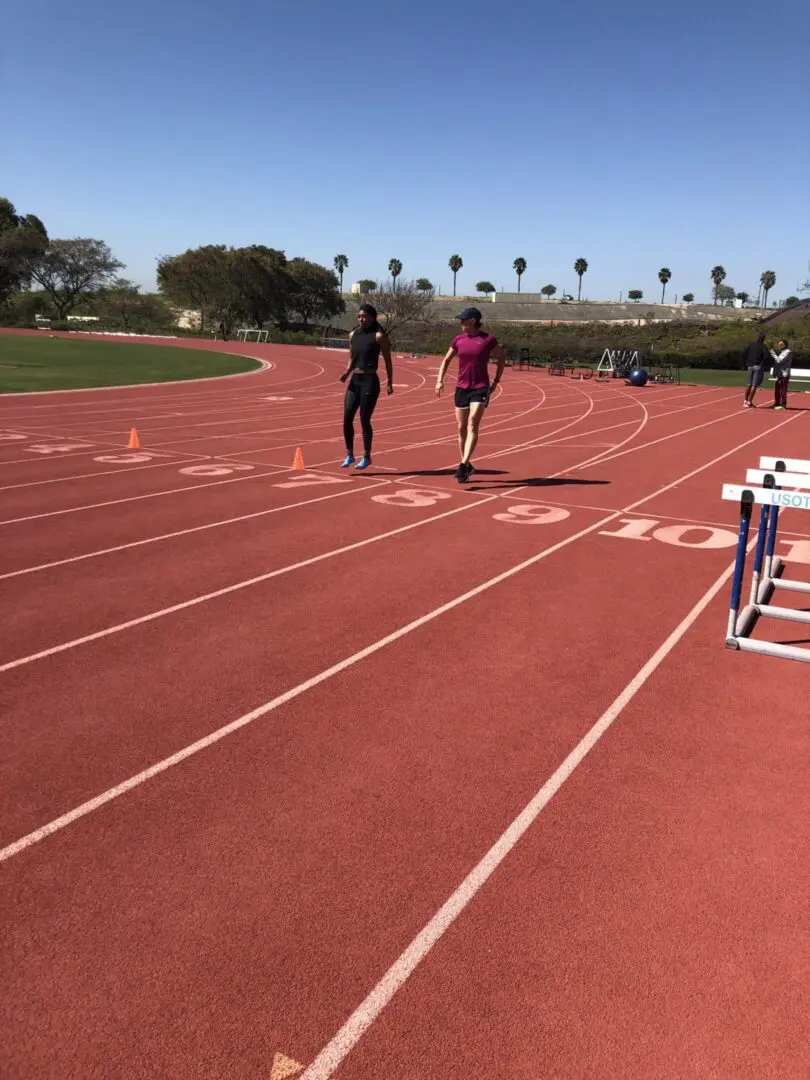Two people running on a sunny outdoor track with palm trees in the background.