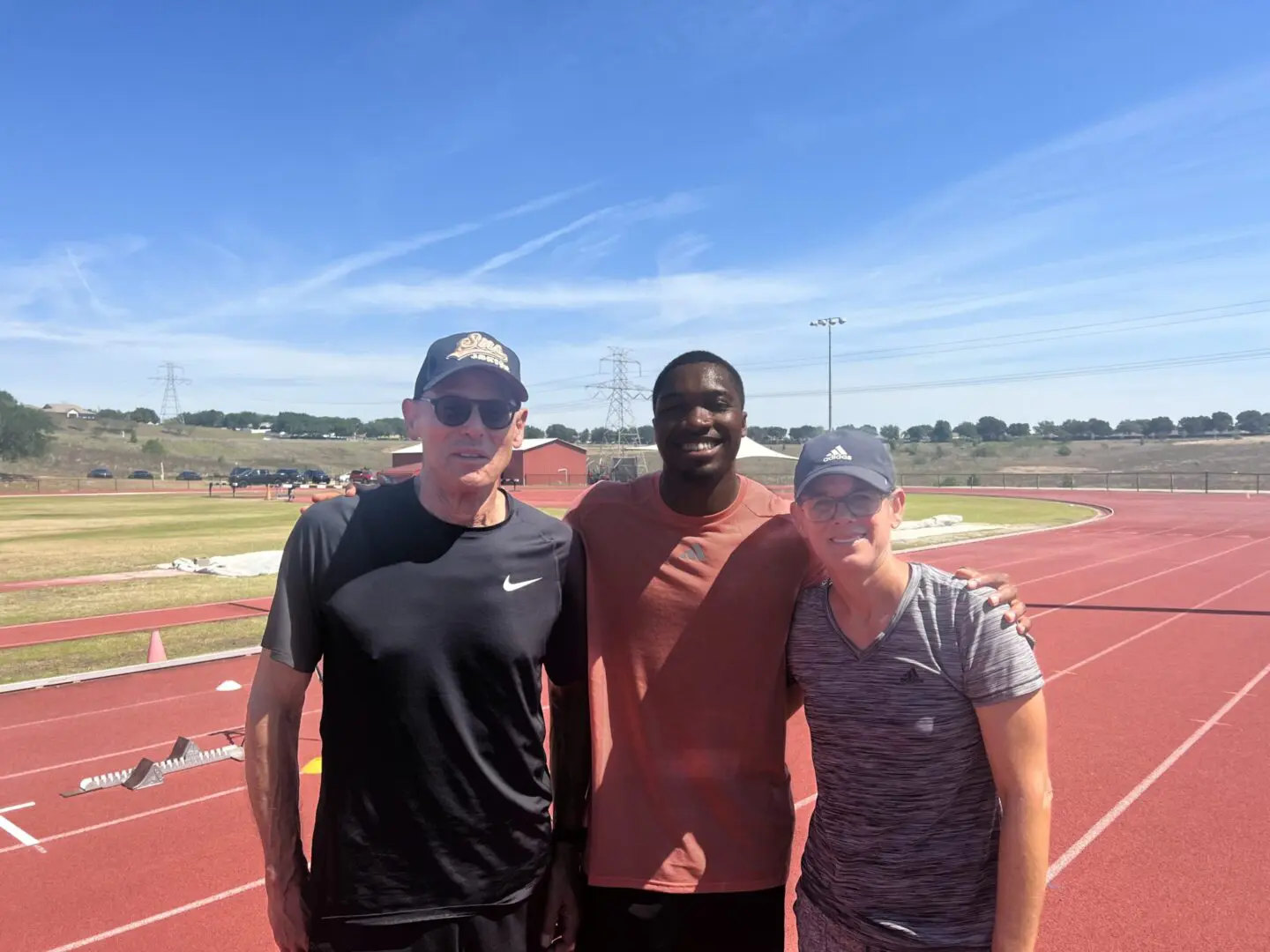 Three people posing on a track field under a clear sky.