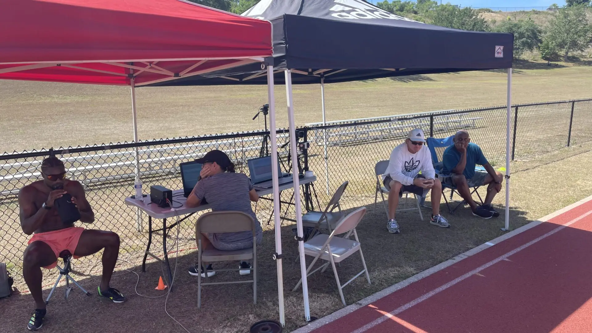 People seated under canopies near a track, some wearing masks.
