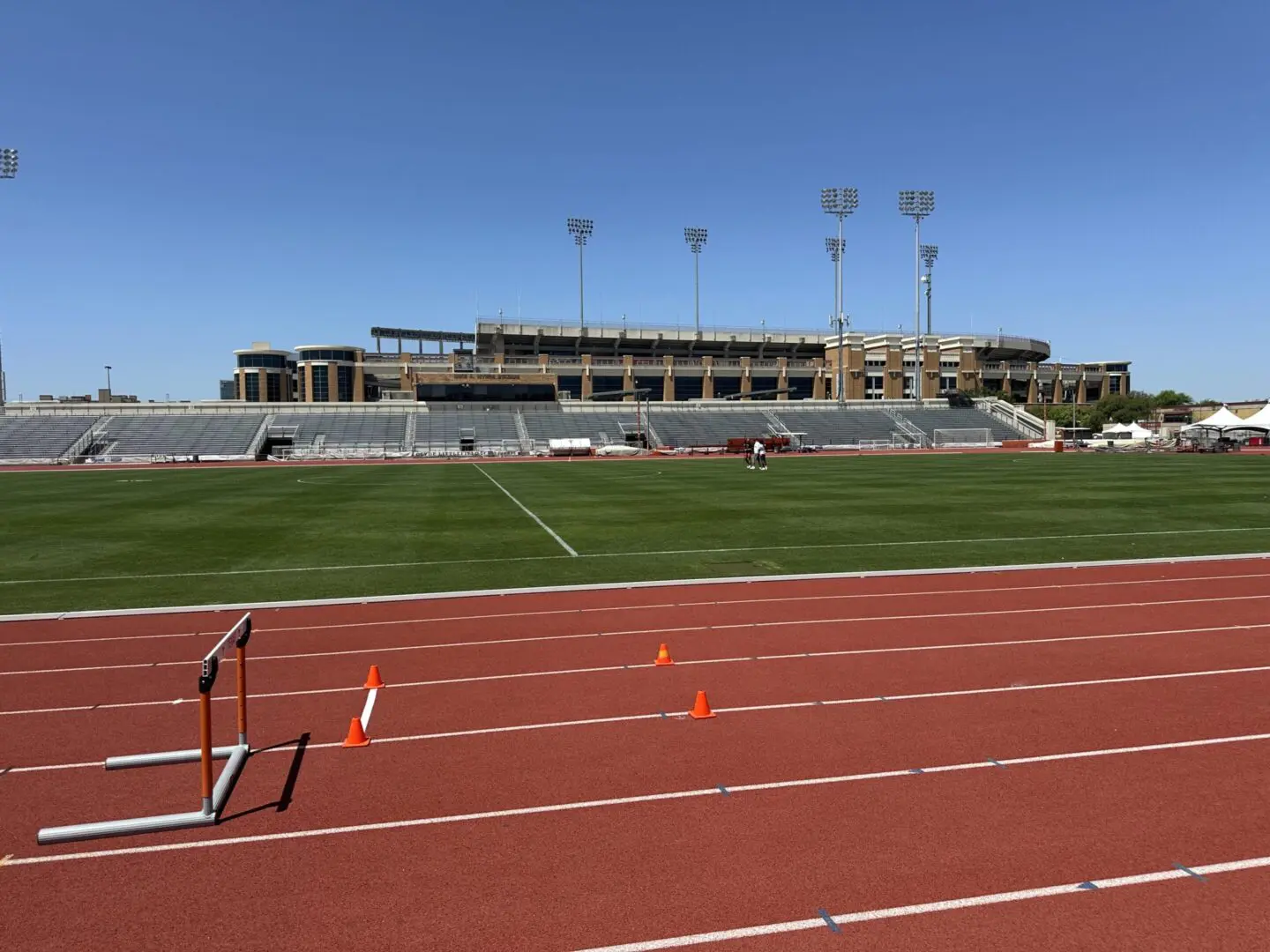 Empty outdoor stadium with a running track and green field under clear blue sky.